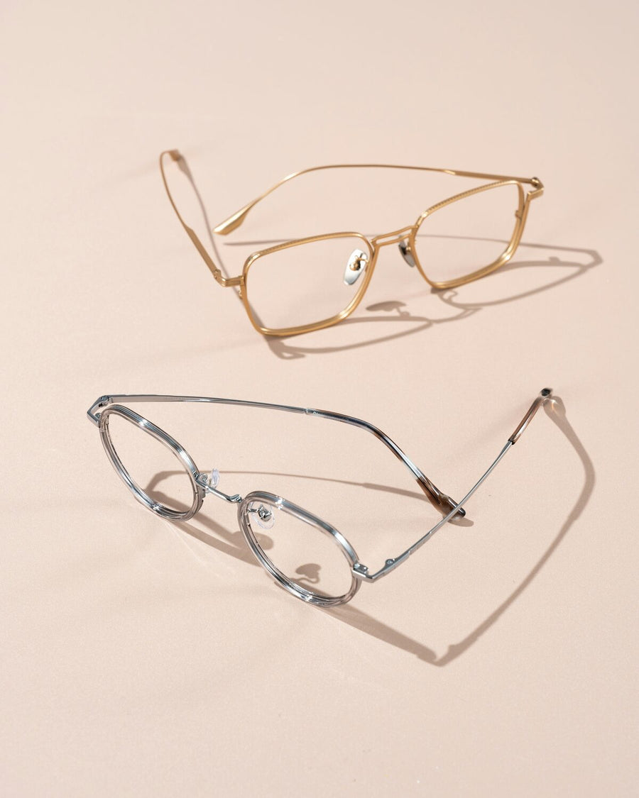 Two pairs of wire-rim eyeglasses, one gold and one silver, resting on a warm beige surface